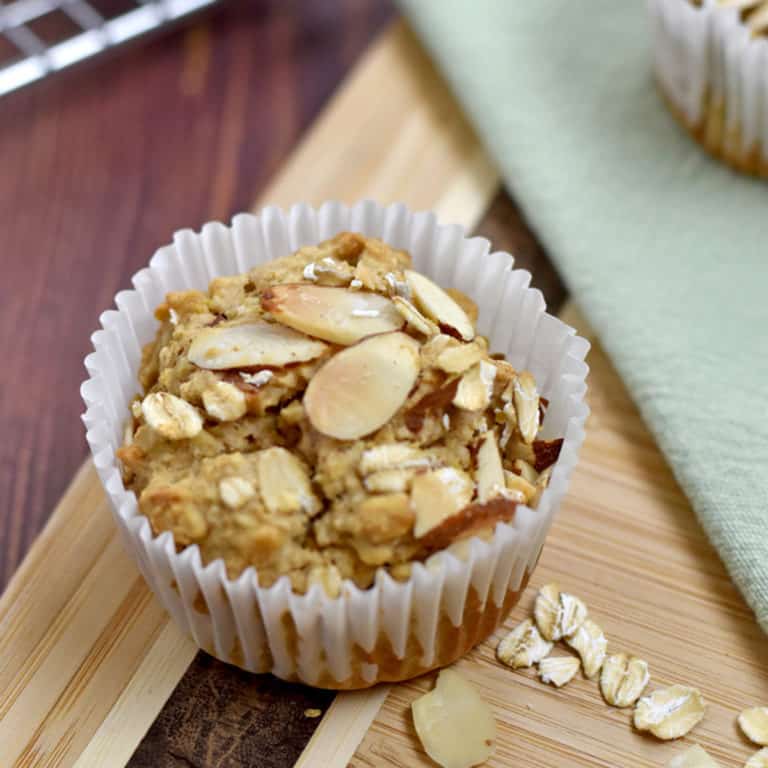 One gluten free oatmeal muffin on a brown cutting board with a few oats and slivered almonds on the cutting board.