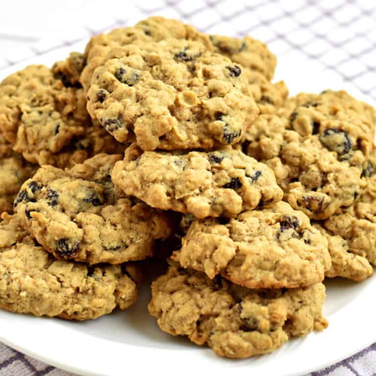 A stack of gluten free oatmeal raisin cookies on a white plate with a purple and white striped kitchen towel under the plate.
