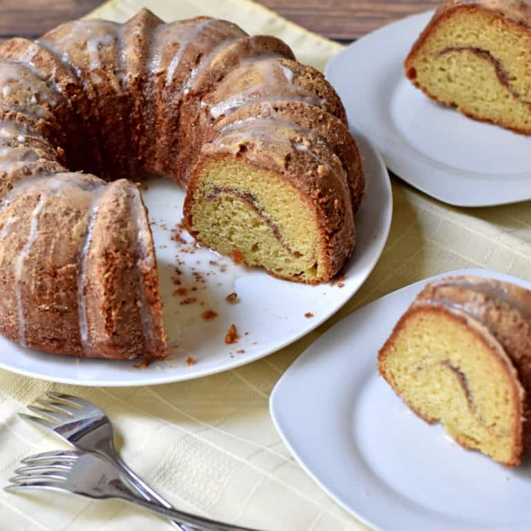 Sour cream coffee cake on a white plate with 2 slices removed. A slice of cake on two separate white plates and two dessert forks in the foreground.