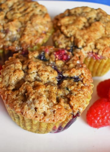 Close up view of three triple berry gluten free muffins and raspberries on a white plate.