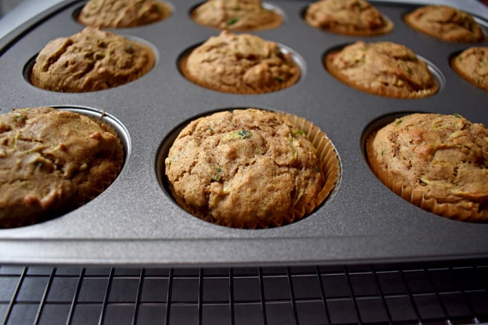 Baked gluten free zucchini muffins in pan on wire rack.