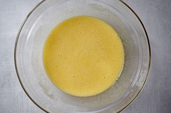 Overhead view of a glass mixing bowl containing unbaked lemon bar filling.