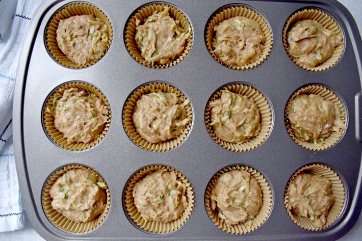 Overhead view of 12-cup muffin pan filled with batter for making gluten free zucchini muffins.