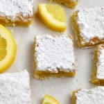 Close up view of a gluten free lemon bar with lemon slices and more lemon bars around it.