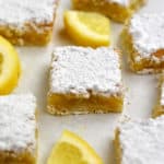 Close up view of a gluten free lemon bar with lemon slices and more lemon bars around it.