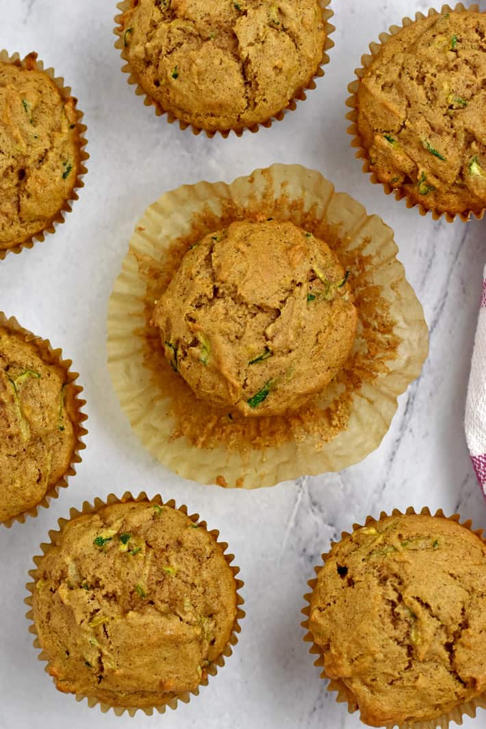 Overhead view of gluten free zucchini muffins on counter top with the paper baking cup peeled back from the muffin in the middle.