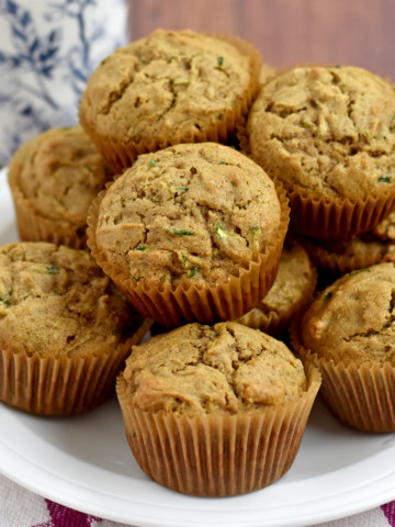 A stack of gluten free zucchini muffins on a round white plate with a blue and white decorative coffee cup in the background.