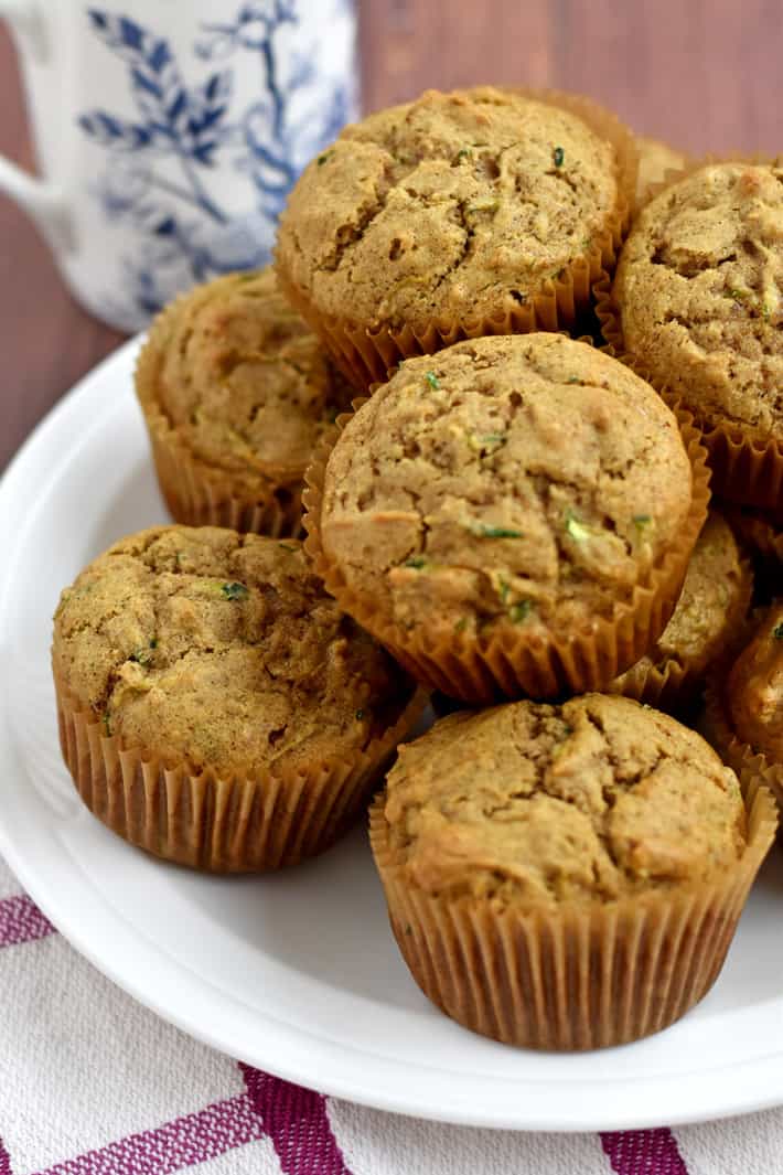 A stack of gluten free zucchini muffins on a round white plate with a blue and white decorative coffee cup in the background.