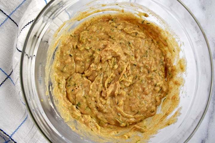 Overhead view of gluten free zucchini bread batter in a glass bowl with a blue and white striped kitchen towel on the left.