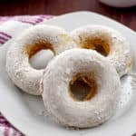 Three gluten free pumpkin donuts on a small white plate with a pink and white striped kitchen towel on the left.
