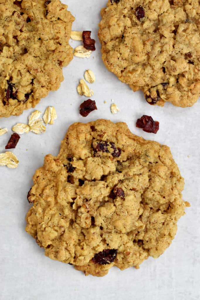 Overhead view of three gluten free cranberry oatmeal cookies and a sprinkling of dried cranberries and oats on a kitchen counter.