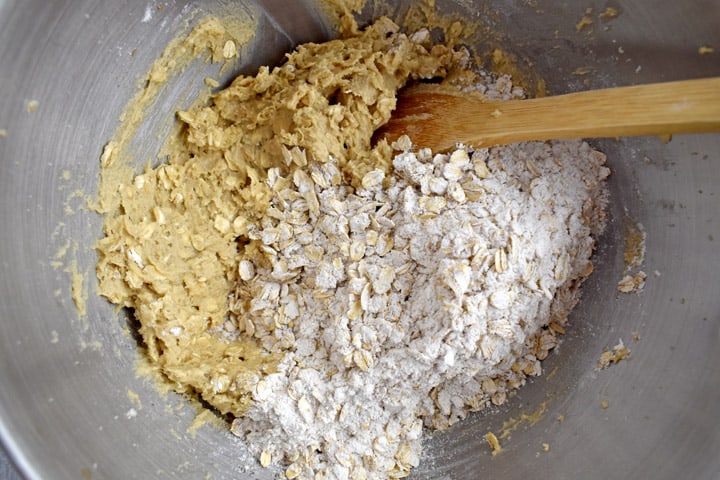 Overhead view of metal mixing bowl with partially mixed cookie dough and wooden spoon.