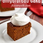 A slice of gluten free gingerbread cake, topped with whipped topping, on a small white plate with more cake in the background and a red and white text overlay near the top.