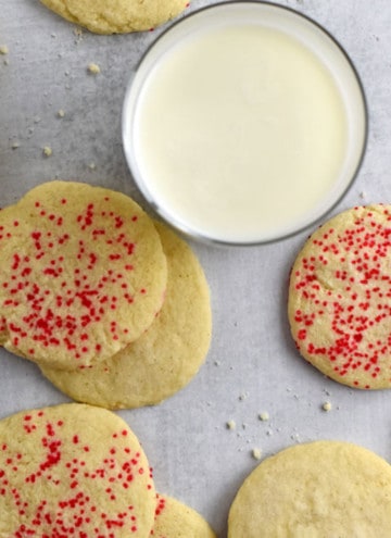 Overhead view of gluten free butter cookies scattered around a glass of milk.