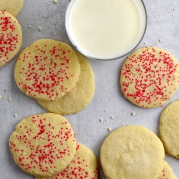 Overhead view of a glass of milk and gluten free butter cookies scattered on parchment paper.