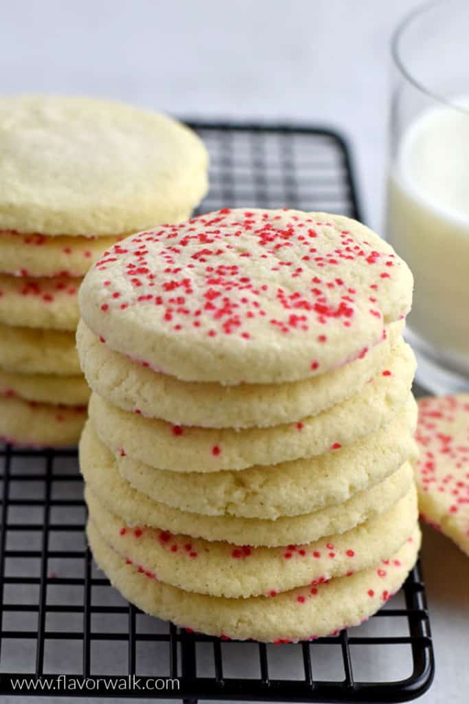 Two stacks of gluten free butter cookies on a black cooling rack with a glass of milk and another cookie on the right.