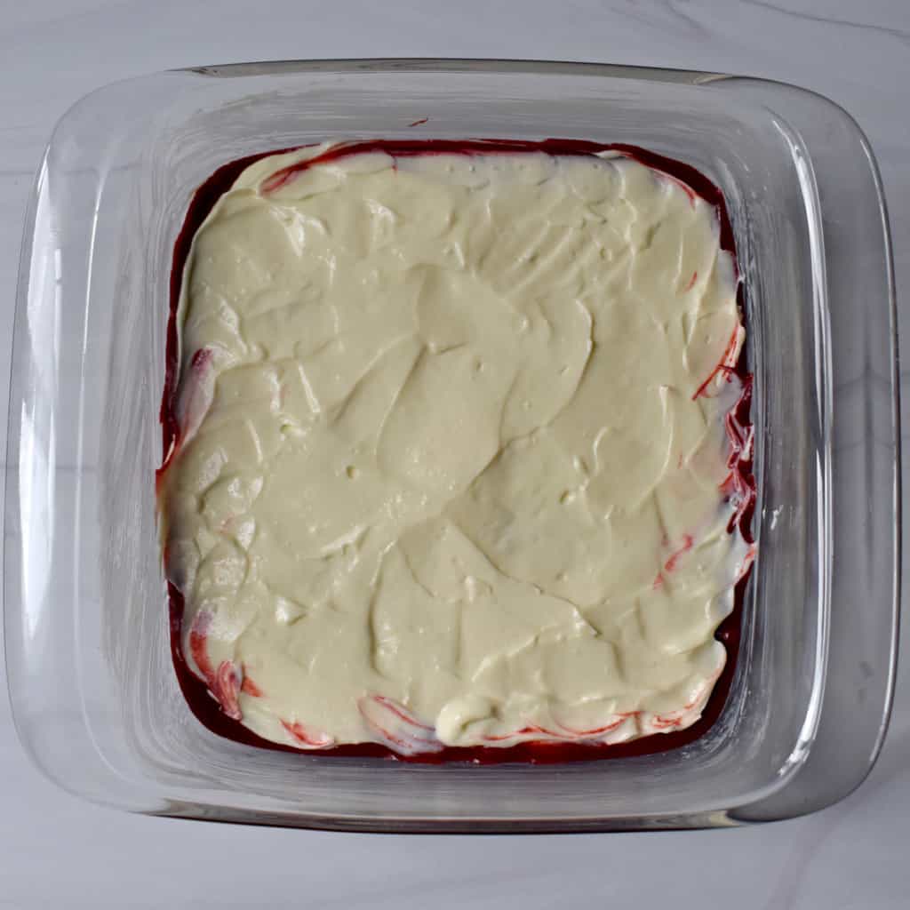 Overhead view of cream cheese layer spread over brownie layer in glass baking pan.