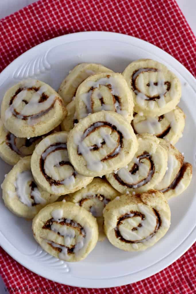 Overhead view of gluten free cinnamon roll cookies on a white plate sitting on a red and white checked kitchen towel.