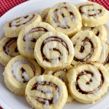 Close up view of a white plate filled with gluten free cinnamon roll cookies on a red and white checked kitchen towel.