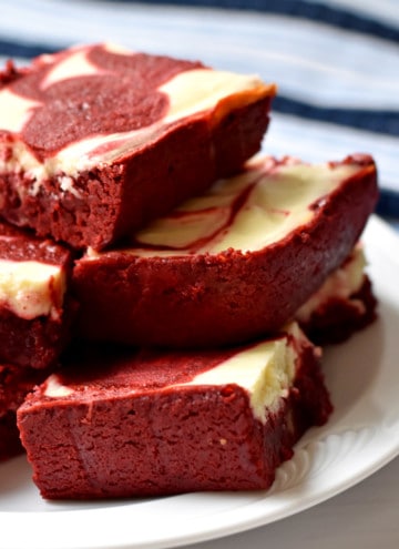 A stack of gluten free red velvet brownies on a round white plate with a blue and white striped kitchen towel in the background.