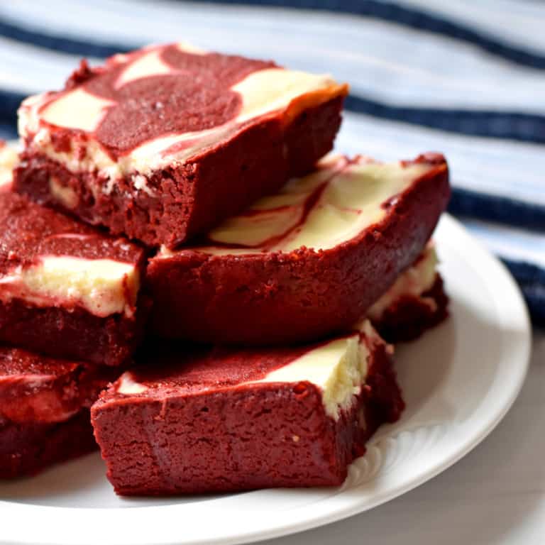 A stack of gluten free red velvet brownies on a round white plate with a blue and white striped kitchen towel in the background.