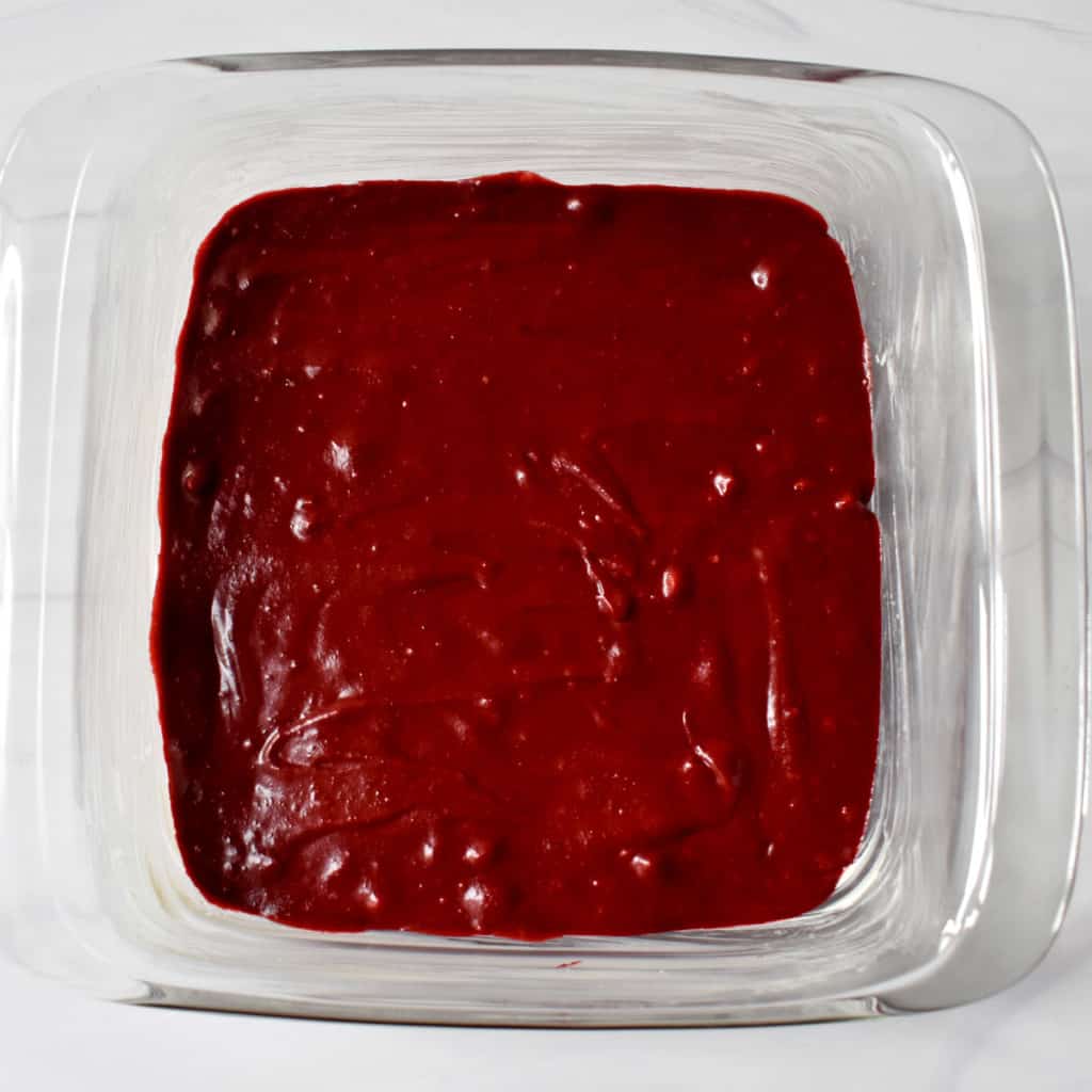 Overhead view of brownie batter layer for making gf red velvet brownies in glass baking pan.