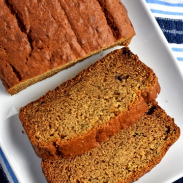 Overhead view of a loaf of gluten free peanut butter banana bread and 2 slices on a white rectangular serving platter sitting on a blue and white striped kitchen towel.