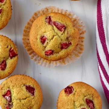 Overhead view of several gluten free strawberry muffins on a kitchen counter with a raspberry and white striped towel on the right.
