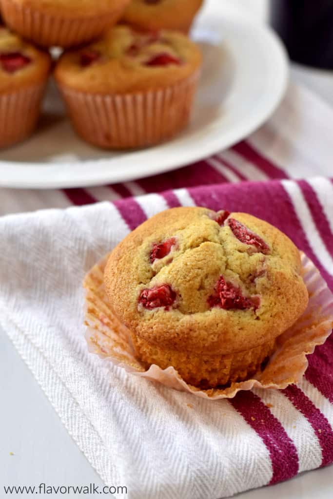 Close up view of one gluten free strawberry muffin on a raspberry and white striped towel with more muffins in the background.