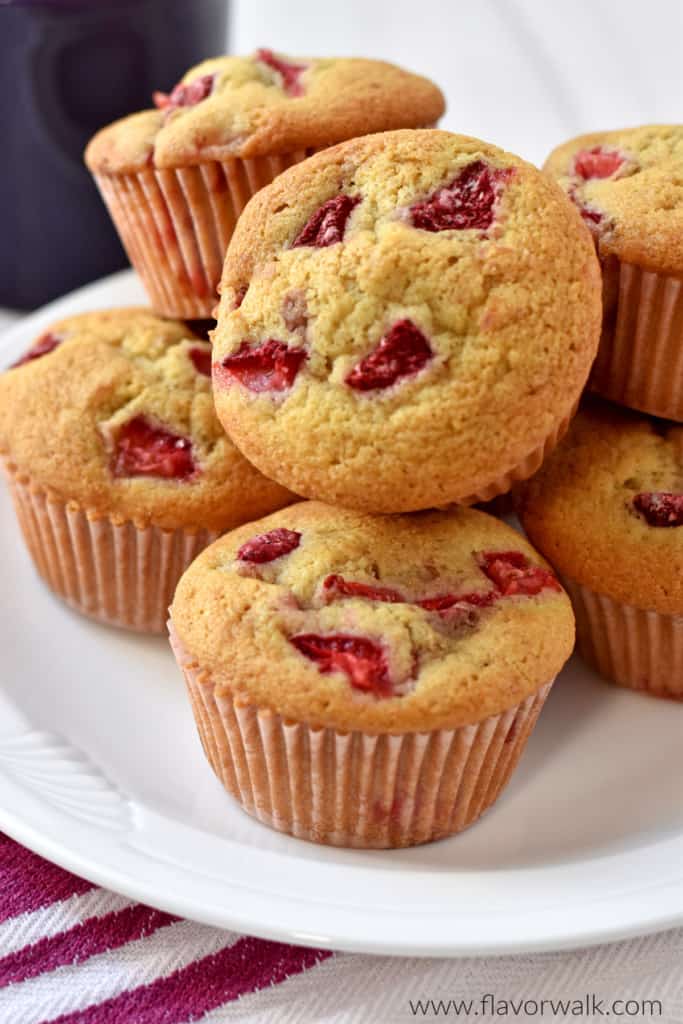 Close up view of a stack of gluten free strawberry muffins on a round white plate with a raspberry and white striped towel under the plate and a purple coffee cup in the background.