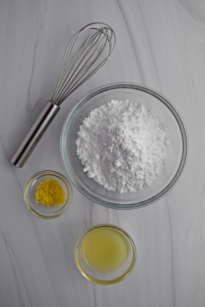 Overhead view of a wire whisk and the ingredients needed to make lemon glaze.