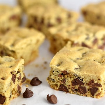 Close up view of chocolate chip cookie bars and a few chocolate chips scattered on parchment paper.