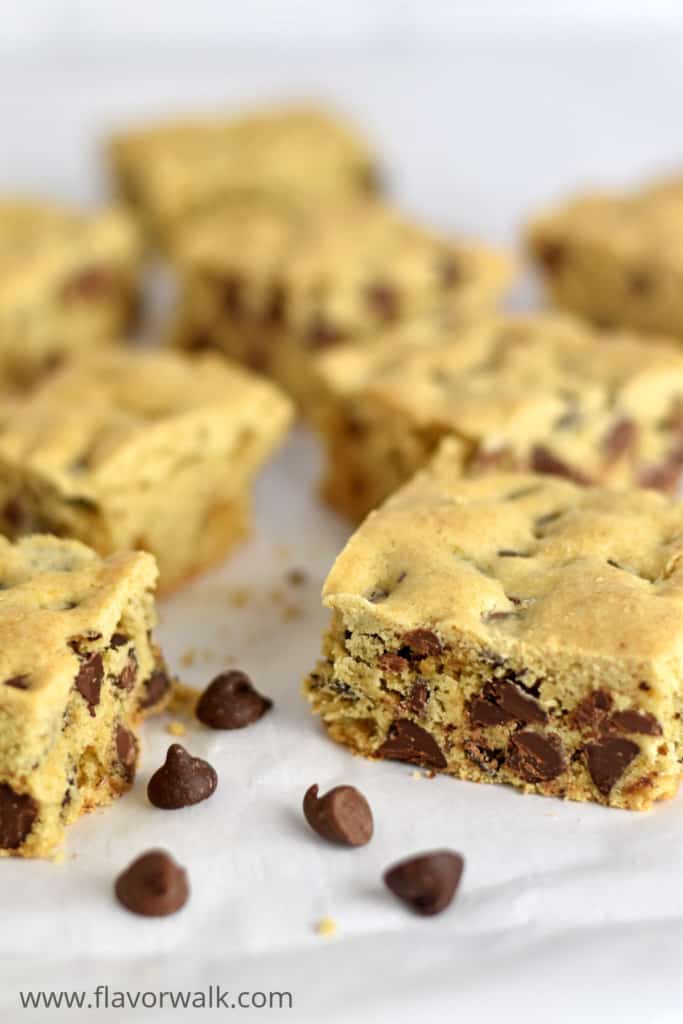 Close up view of chocolate chip cookie bars and a few chocolate chips scattered on parchment paper.