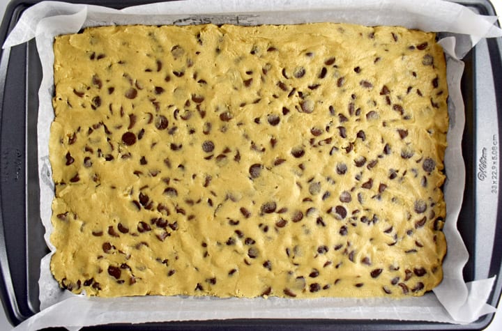 Overhead view of a pan of unbaked dough for chocolate chip cookie bars.