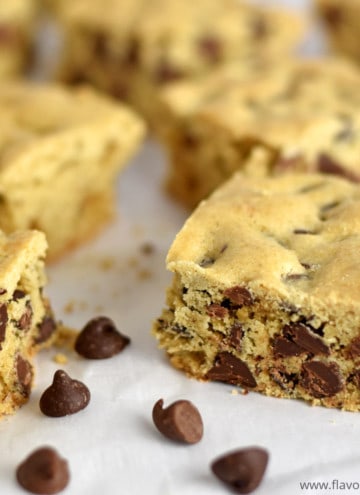 Close up view of gluten free cookie bars and a few chocolate chips scattered on parchment paper.