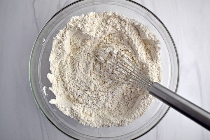 Overhead view of glass mixing bowl containing gluten free flour blend, baking powder, and salt, whisked together with wire whisk.