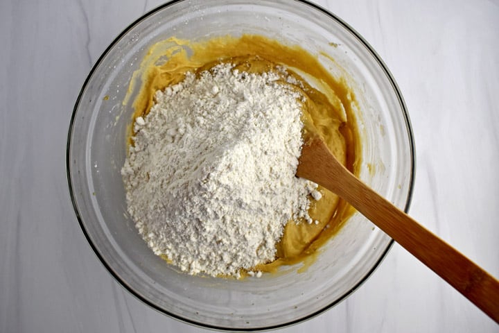 Overhead view of glass mixing bowl with gluten free flour mixture waiting to be stirred into cookie dough batter and wooden spoon