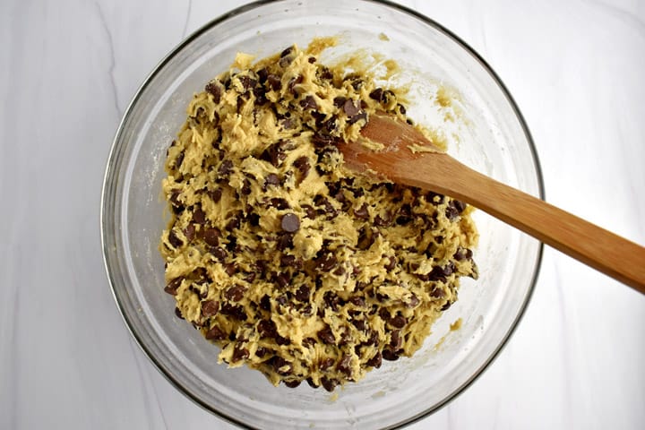 Overhead view of glass mixing bowl containing gluten free chocolate chip cookie bar dough and a wooden spoon.