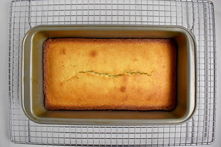 Overhead view of baked lemon pound cake in pan, cooling on wire rack.