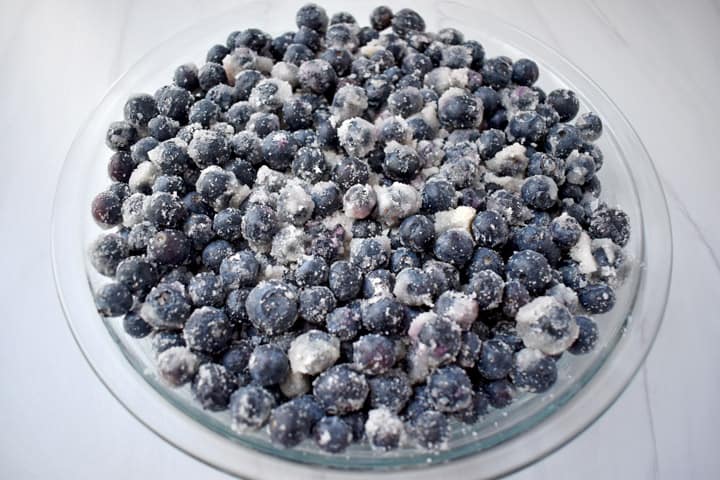 Glass pie dish filled with unbaked blueberry crisp filling.