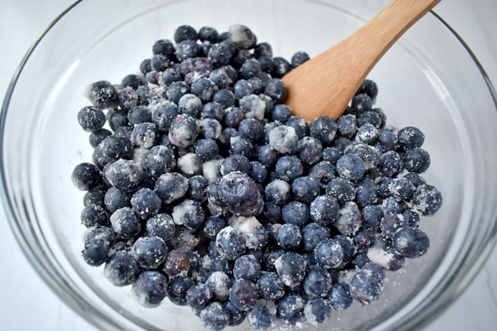 Overhead view of blueberry filling ingredients tossed together in a glass mixing bowl.