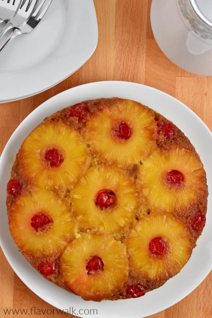 Overhead view of gluten free pineapple upside-down cake on white plate on counter along with dessert plates, forks, and coffee pot.