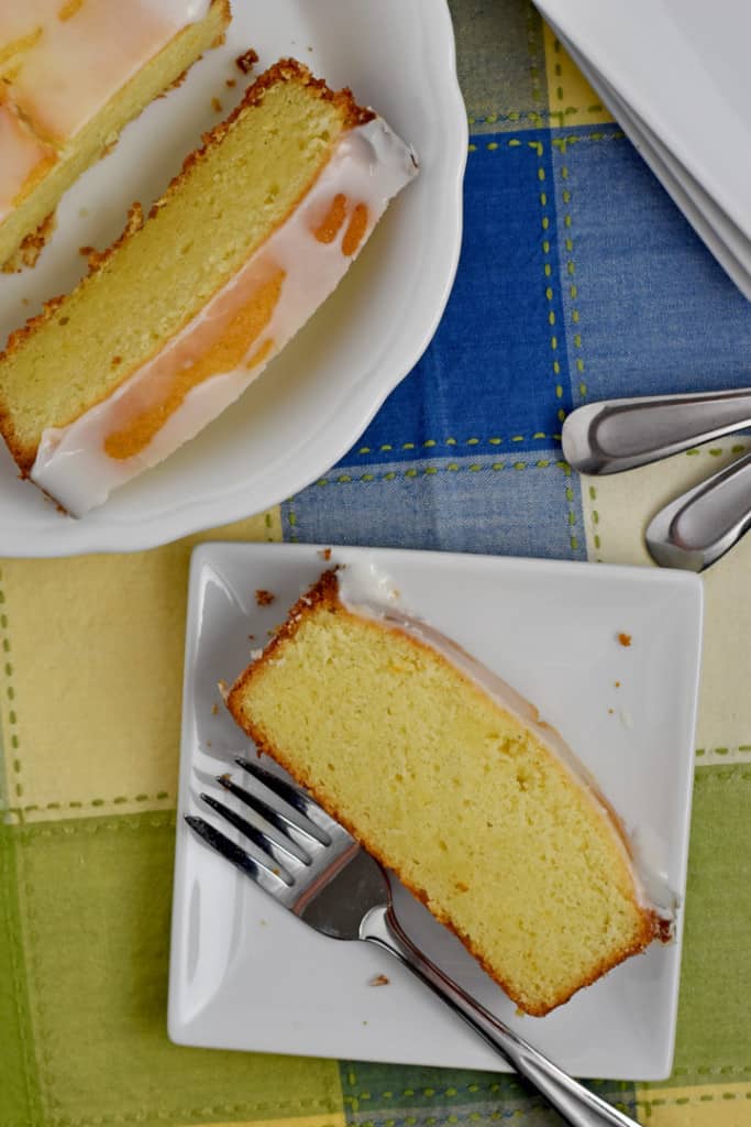 Overhead view of a slice of gluten free lemon pound cake and a fork on a small white plate with more cake, forks, and plates in the background.