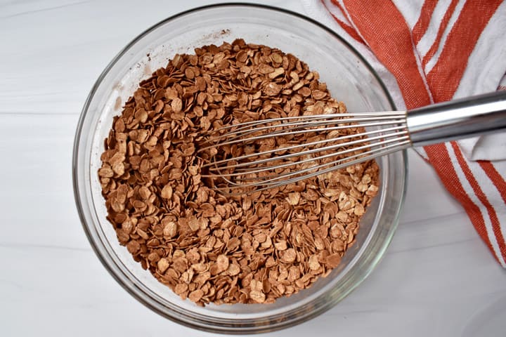 Overhead view of the dry ingredients for making chocolate peanut butter oatmeal cups whisked together in a glass mixing bowl with a red and white striped kitchen towel on the right.