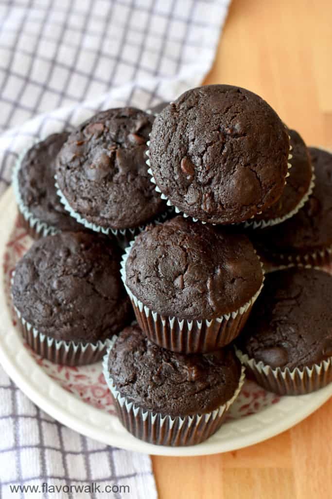 Close up view of a stack of gluten free chocolate zucchini muffins on a round plate with a purple and white striped kitchen towel on the left.