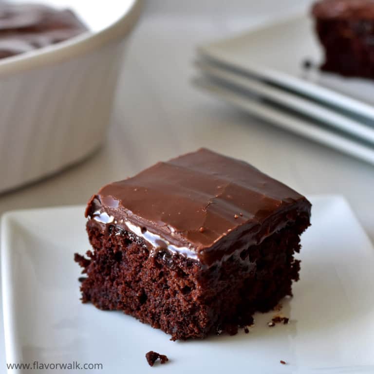 Close up view of one gluten free zucchini brownie on a small white plate with more brownies in the background.