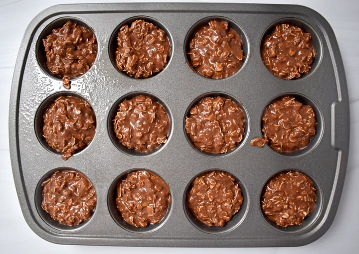 Overhead view of unbaked chocolate peanut butter oatmeal cup batter in a metal muffin pan.