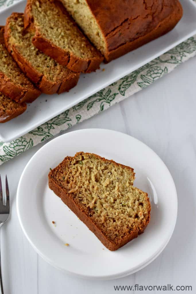 A slice of gluten free zucchini banana bread on a stack of 2 round plates with a fork on the left and more bread in the background.