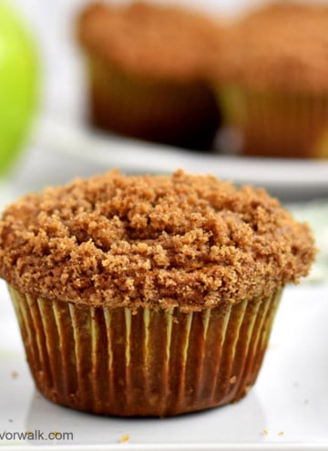 Close up view of one gluten free apple muffin on a small white plate with a granny smith apple and more muffins in the background.