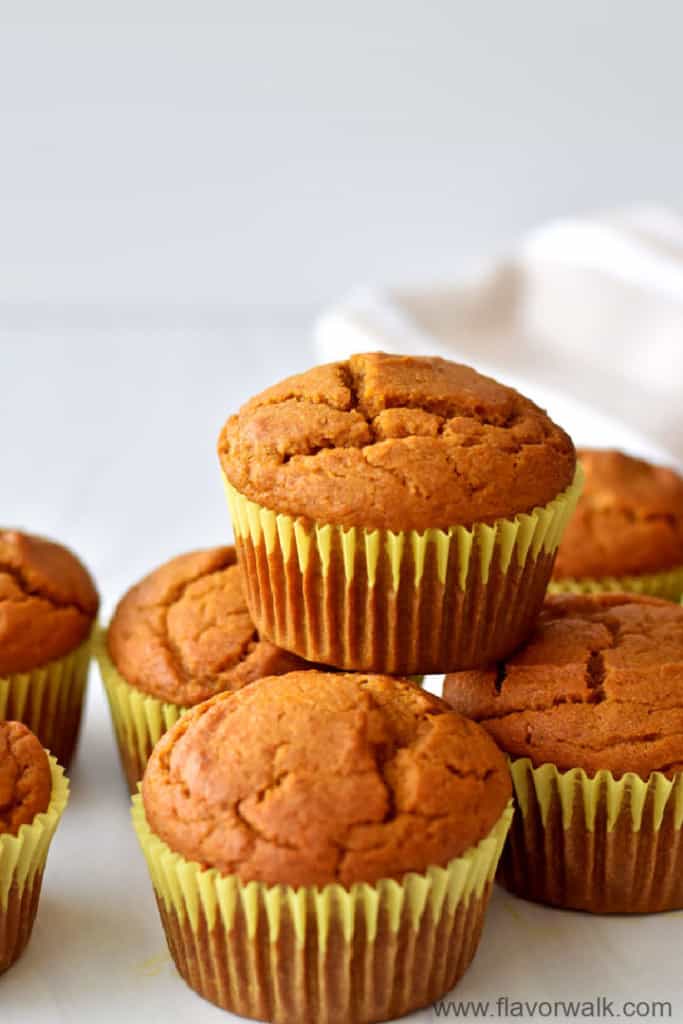 Close up view of one gluten free pumpkin muffin stacked on other pumpkin muffins with a tan and white striped kitchen towel in the background.